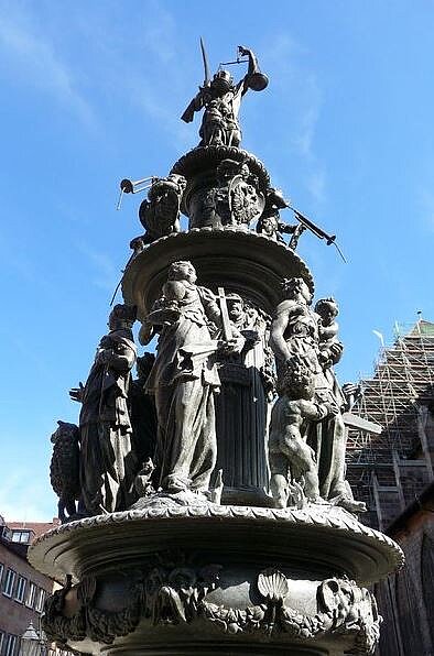 Detailansicht des bronzenen Tugendbrunnens mit seinen mehrstöckig angeordneten allegorischen Figuren, gekrönt von der Justitia mit Schwert und Waage.