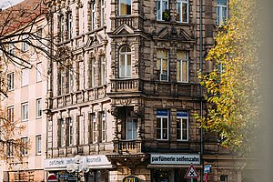 Historische Eckfassade mit Parfümerie Seifenzahn am Jakobsmarkt, verziert mit Steinornamenten, Rundbogenfenstern und Ladenschildern in belebter Straßenkreuzung.