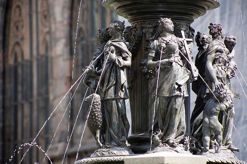 Farbige Nahaufnahme der Bronzeskulpturen, die Wasser aus ihren Brüsten in das Becken speien.