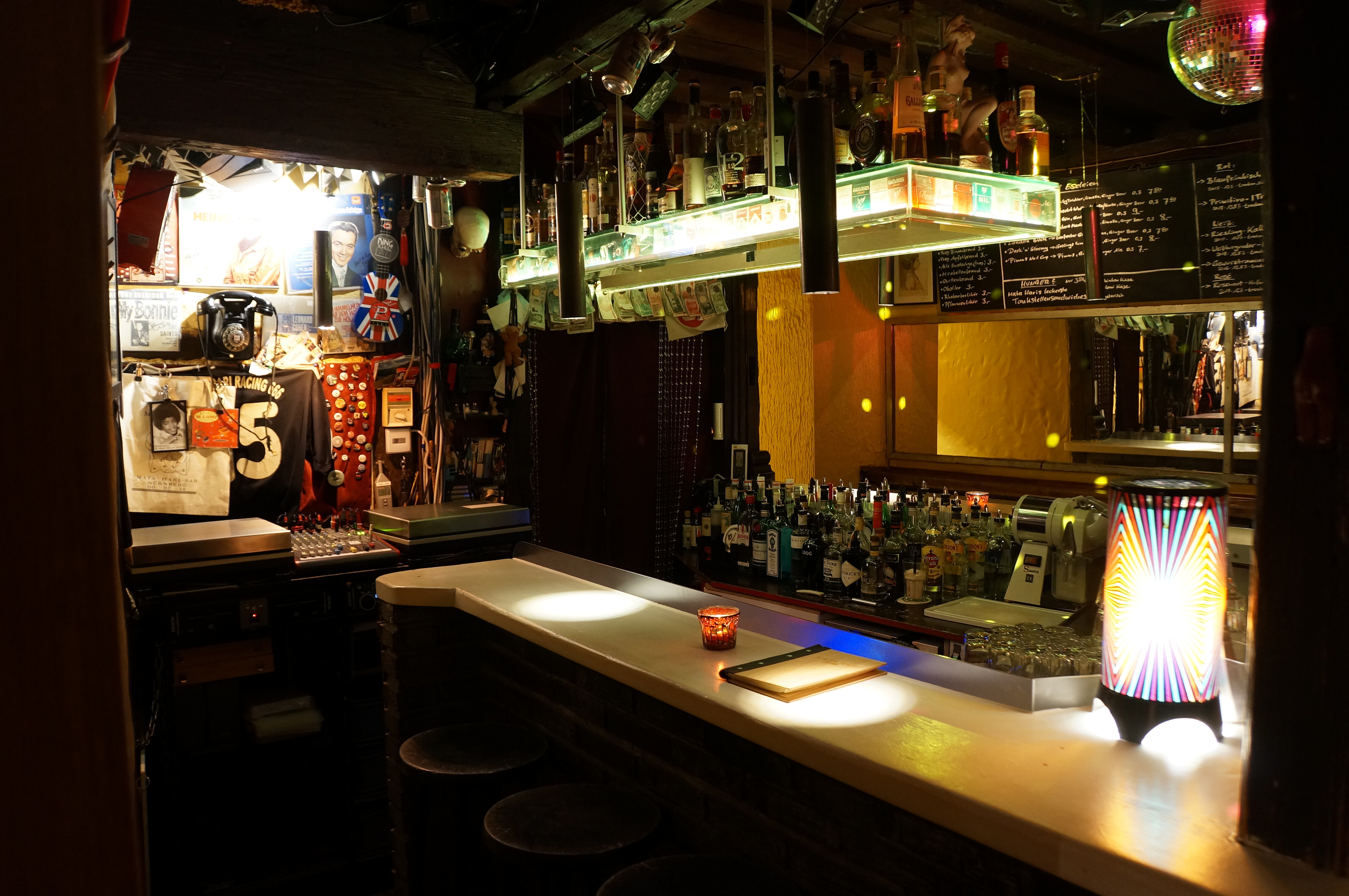 In der Mata Hari Bar sind hinter dem beleuchteten Tresen zahlreiche Spirituosenflaschen aufgereiht, während die Wände mit Postern, einem alten Telefon und verschiedenen Musik-Erinnerungsstücken dekoriert sind.