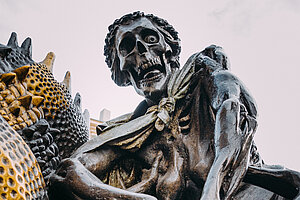 Dramatische Figurengruppe des Ehekarussells am Jakobsmarkt mit skelettartigen Gestalten und expressiven Formen vor bewölktem Himmel.