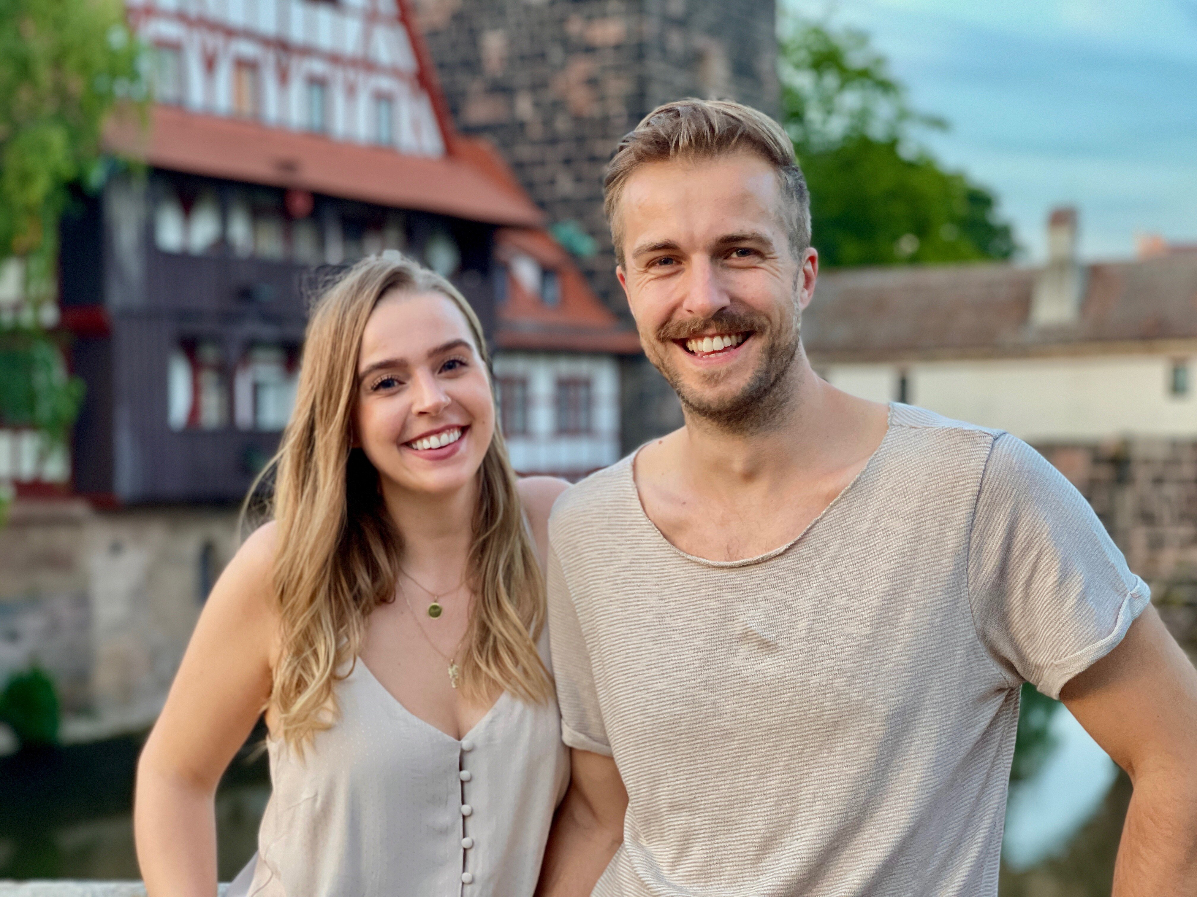Kristof und Lena stehen lächelnd vor historischem Fachwerk und Wasser im Nürnberger Quartier.