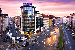 Park Inn Hotel mit geschwungener Glasfassade an belebter Straßenkreuzung vor farbigem Abendhimmel.