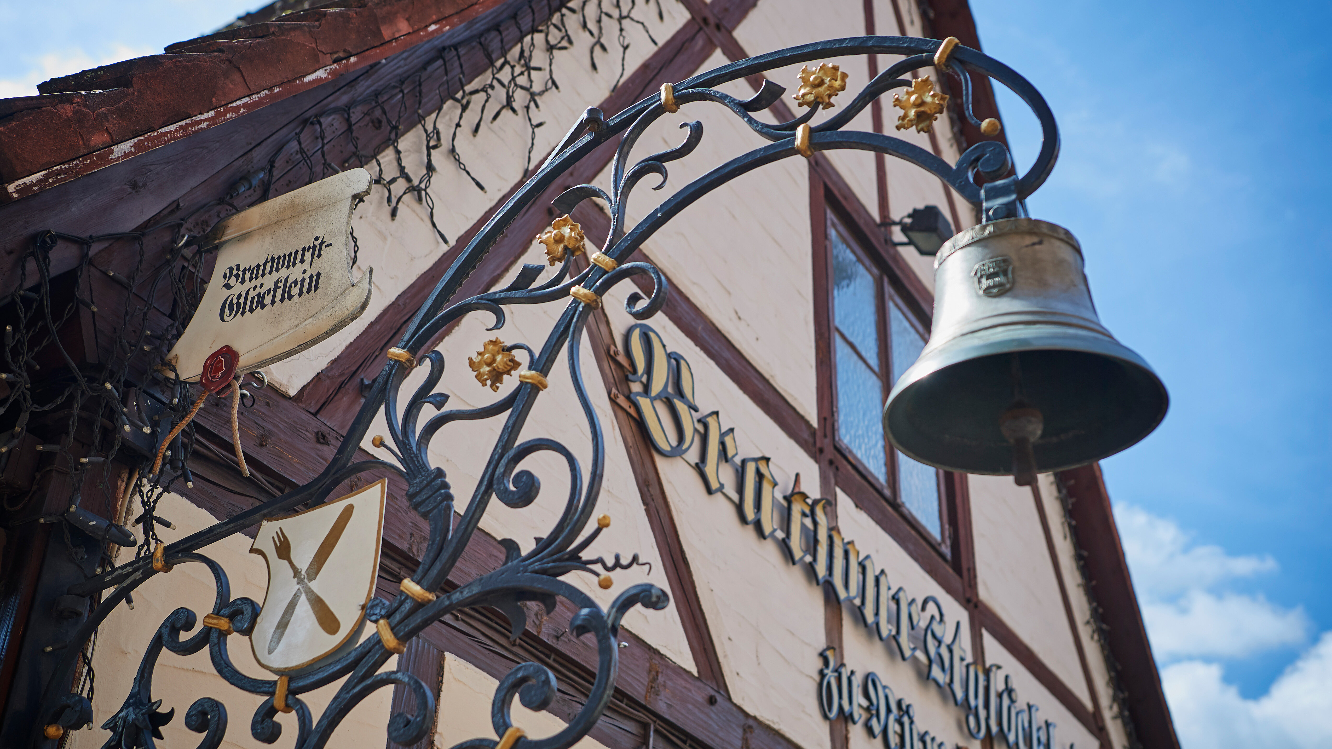 Ein schmiedeeisernes Schild mit Glocke und Wappen hängt vor der Fachwerkfassade des Restaurants „Bratwurst-Glöcklein“ in Nürnberg.