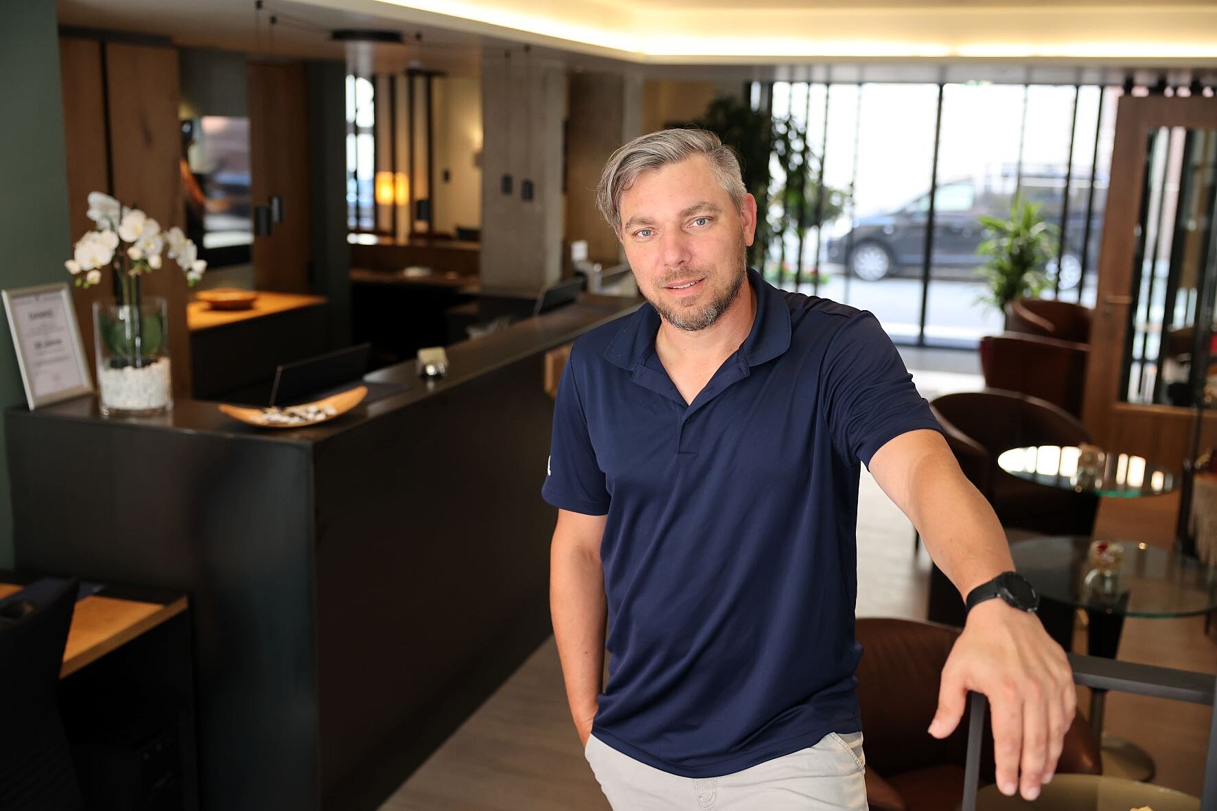 Thorsten Hofmann Thorsten Hofmann steht in einem dunkelblauen Poloshirt in der modern gestalteten Lobby des Hotels am Jakobsmarkt.