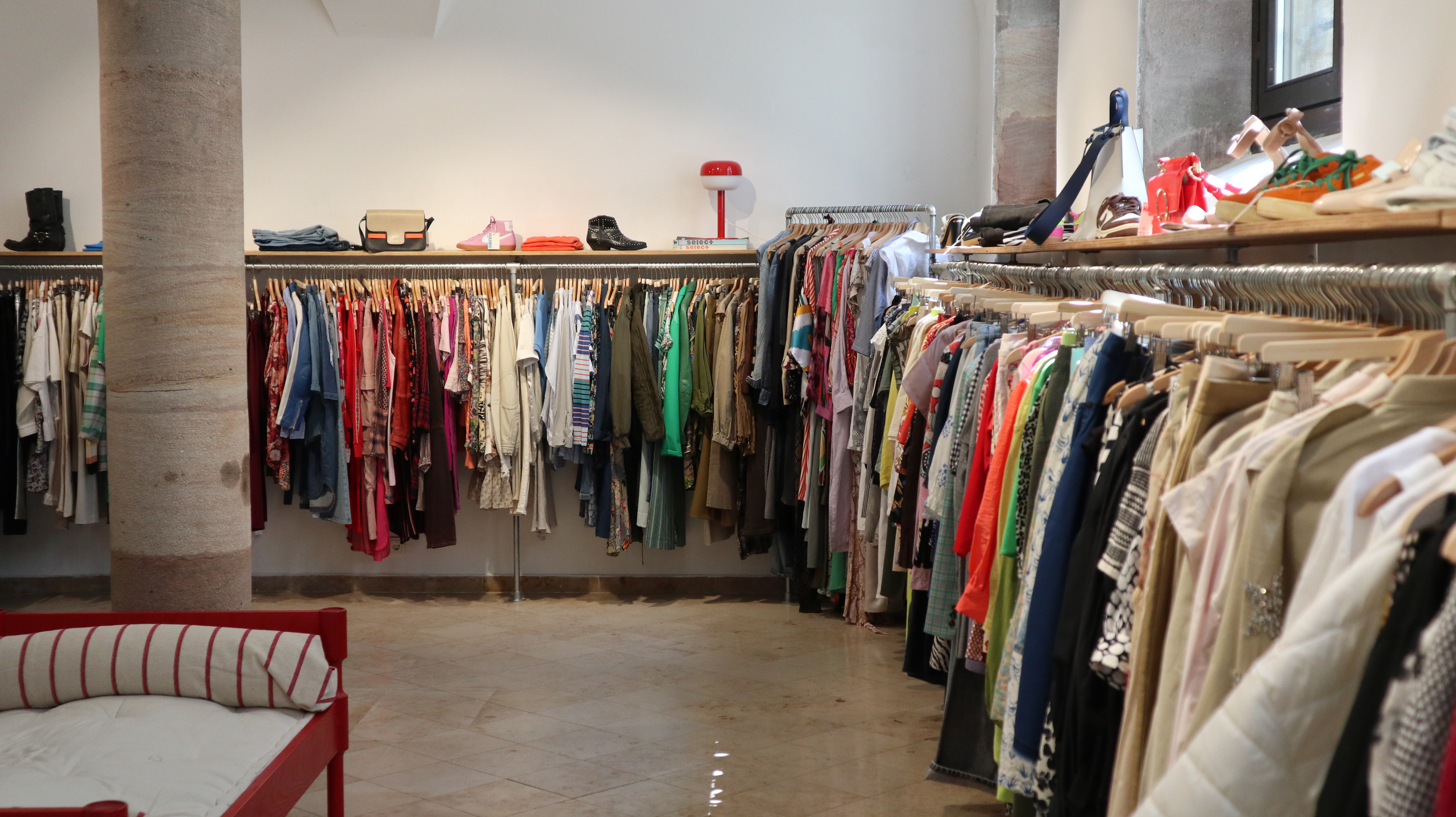 Innenraum eines Secondhand-Ladens mit Kleiderstangen voller bunter Kleidung und Schuhen auf Regalen an den Wänden