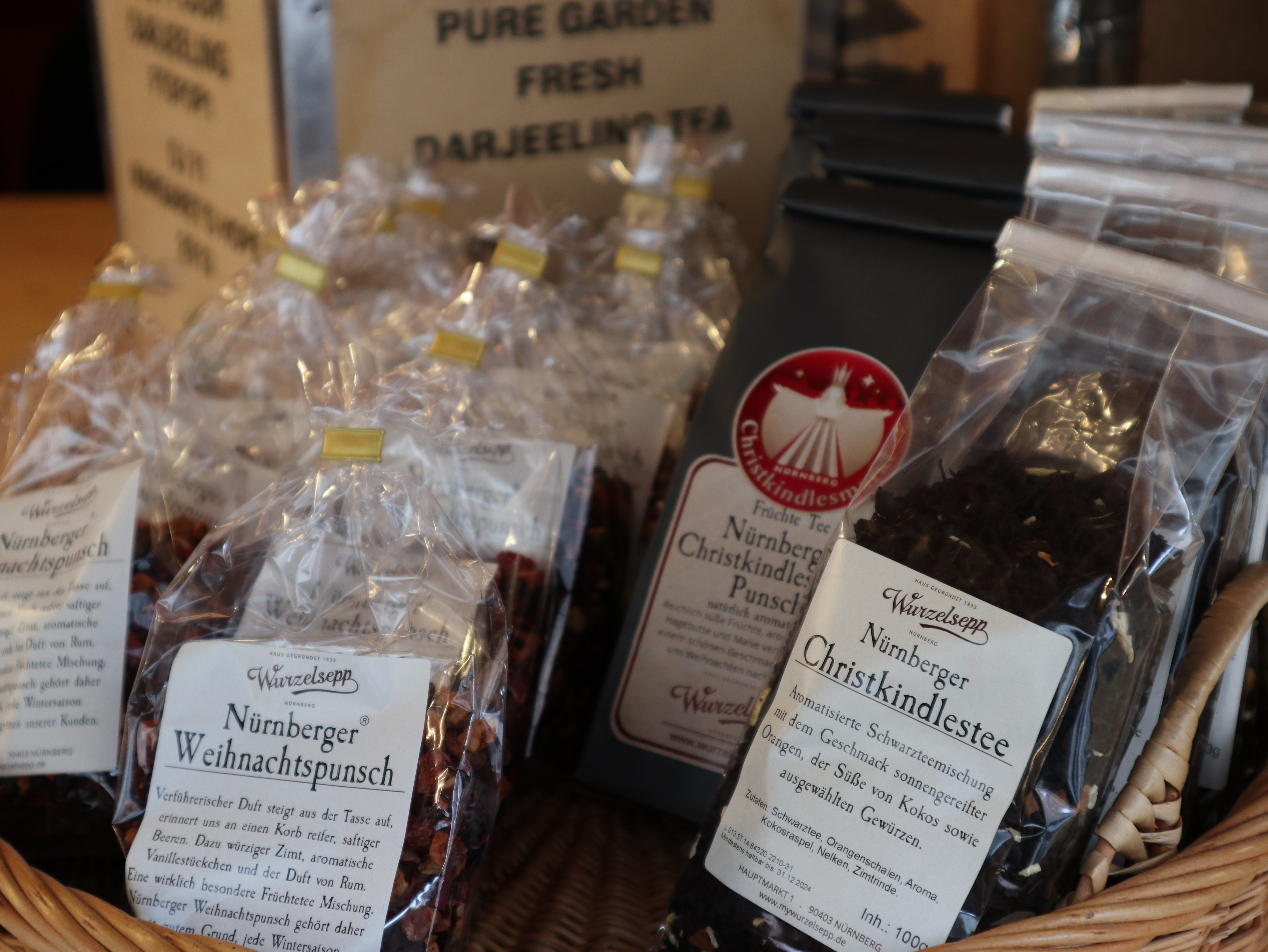 In einem Weidenkorb sind verschiedene Teemischungen von Wurzel-Sepp präsentiert, darunter der „Nürnberger Weihnachtspunsch“ und der „Nürnberger Christkindlestee“ in Klarsichtbeuteln sowie eine Packung „Nürnberger Christkindlespunsch“.